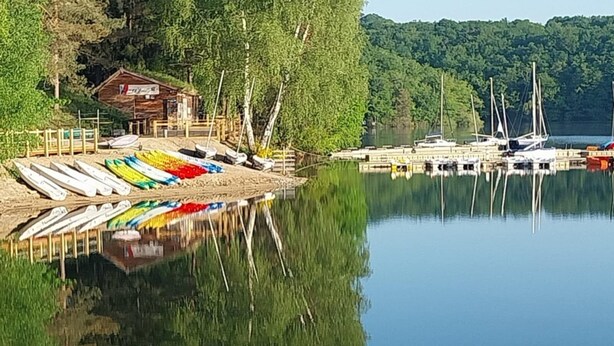 En stilla sjö med förtöjda båtar, en träbrygga och en liten byggnad.