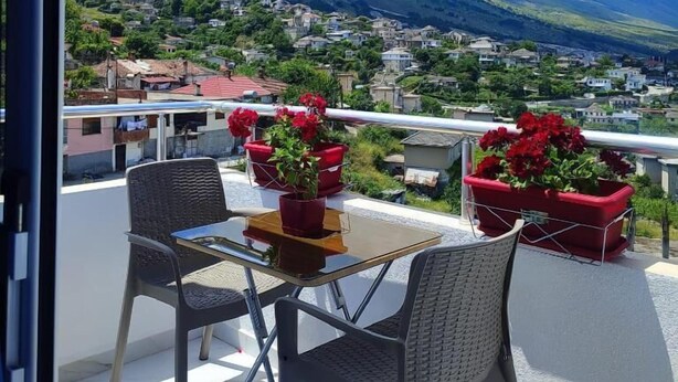 A balcony with a table and chairs, overlooking a mountainous landscape with a village below. - Vladimir Estate (Gjirokastër)