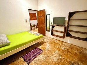 Una habitación con una cama, un televisor en un estante, un espejo y una puerta que da a otra habitación.