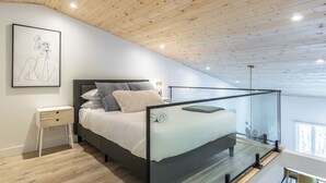 Un dormitorio moderno con techo inclinado, cama con recinto de vidrio, mesita de noche y una obra de arte enmarcada en la pared.