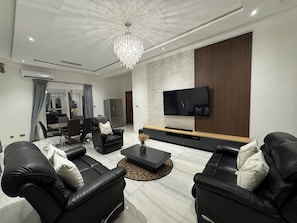 A modern living room with a flat-screen TV, leather sofas, a coffee table, and a chandelier. - Ayan Villas  luxurious One bedroom penthouse with a beach view! (Oshiyie)