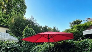 Un patio con dos sillas azules y una sombrilla roja.