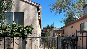 Un edificio residencial con entrada protegida por un portón, una escalera visible y cielo despejado.