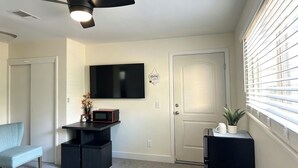 Una sala de estar moderna con ventilador de techo, televisor de pantalla plana, microondas, puerta y ventana con persianas.