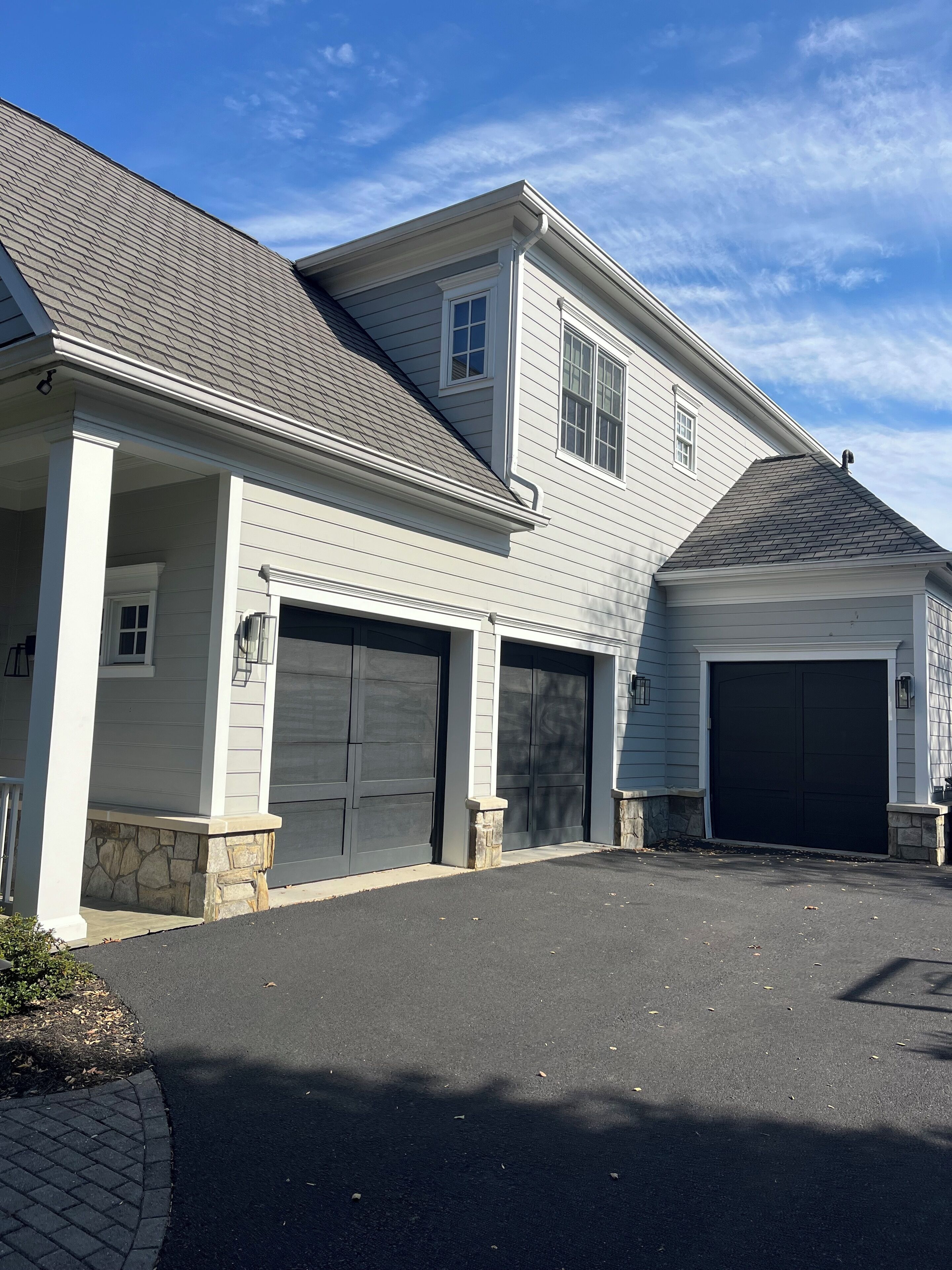 Une maison à deux étages avec un garage, des fondations en pierre et un porche couvert.