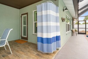 A covered porch with a striped shower curtain, a chair, and a door with shutters. - 3BR Coastal Retreat | Heated Pool + Game Room (Bradenton)