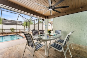 Un patio couvert avec une piscine, des sièges d’extérieur et un ventilateur de plafond.