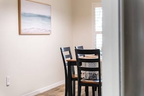 Un coin repas avec une table et des chaises, un tableau accroché au mur et une fenêtre avec des stores.
