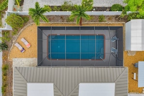 An aerial view of a swimming pool surrounded by a deck area with lounge chairs and palm trees. - 3BR Coastal Retreat | Heated Pool + Game Room (Bradenton)