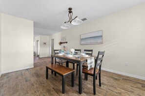 A dining area with a wooden table and chairs, a ceiling light fixture, and a painting on the wall. - 3BR Coastal Retreat | Heated Pool + Game Room (Bradenton)