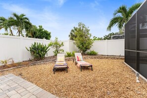 A backyard with two lounge chairs, a white fence, and various plants. - 3BR Coastal Retreat | Heated Pool + Game Room (Bradenton)