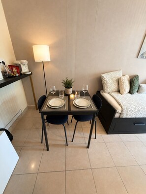 A dining area with a table set for two, a lamp, and a bed with pillows. - Studio apartment in northern Lyon, near the stadium and the LDC Arena (Meyzieu)