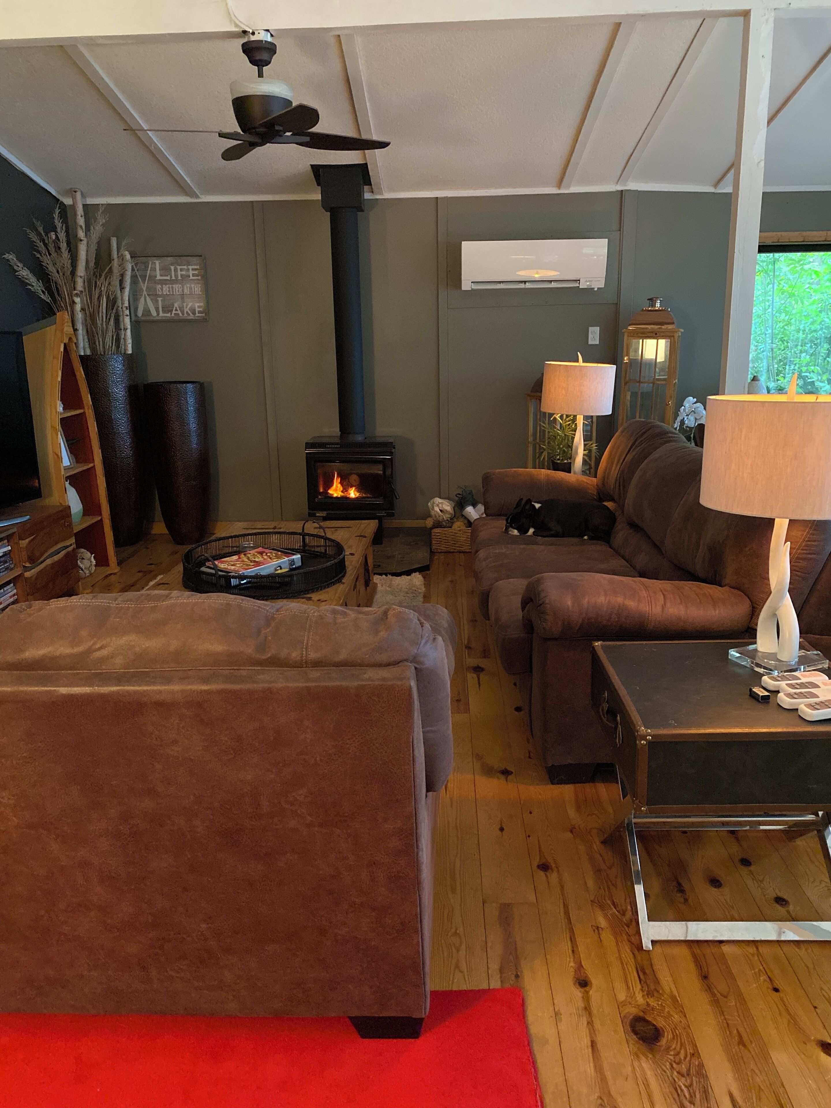 A cozy living room with a fireplace, brown sofas, a red rug, and a ceiling fan.