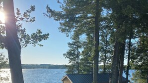 A lakeside cabin with a deck, surrounded by trees and overlooking a body of water.