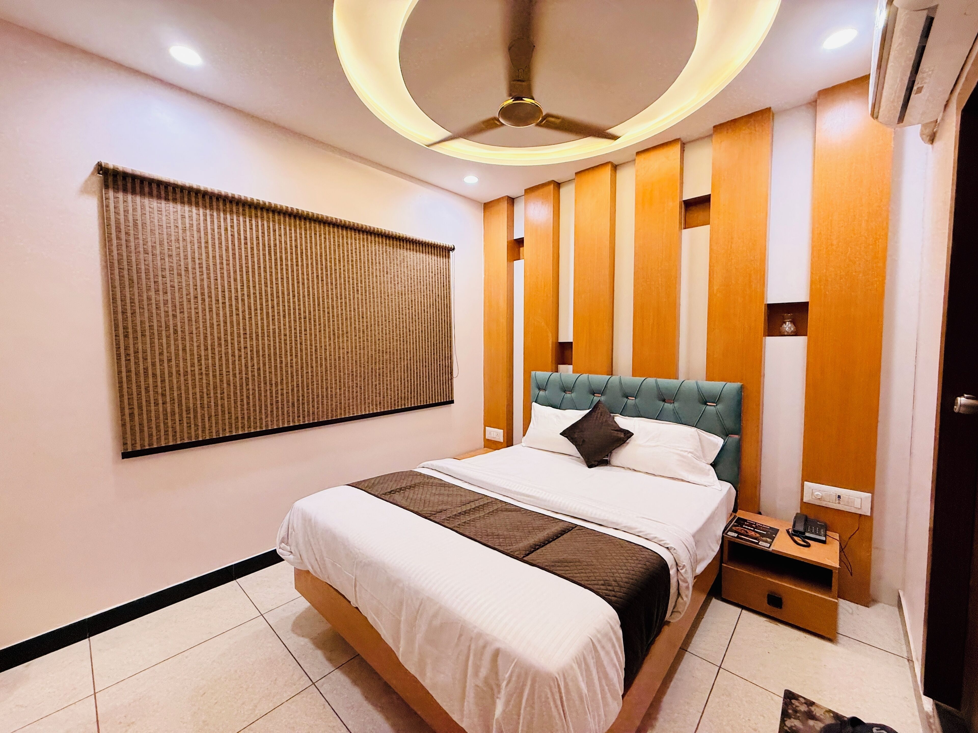Ein modernes Hotelzimmer mit einem großen Bett, einem Deckenventilator, einer Wandklimaanlage und einem Nachttisch mit Telefon und Lampe.