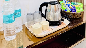 A hotel room with a marble wall, a black kettle, two water bottles, two glasses, and a tray with two cups and a basket of snacks. - Hotel Hira Palace (Ujjain)