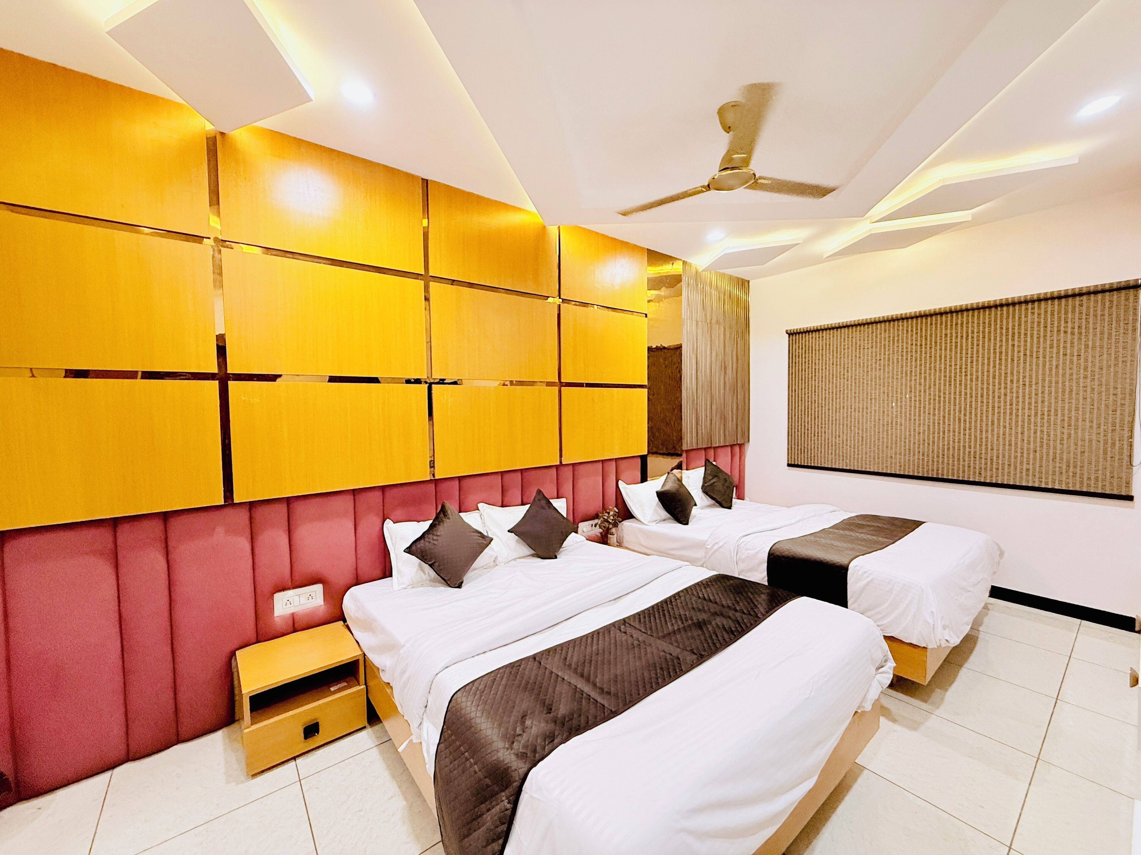 A hotel room with two beds, a ceiling fan, and a large window with blinds.