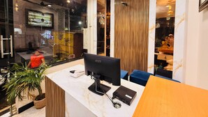 A reception desk with a computer, a plant, and a wooden accent wall. - Hotel Hira Palace (Ujjain)