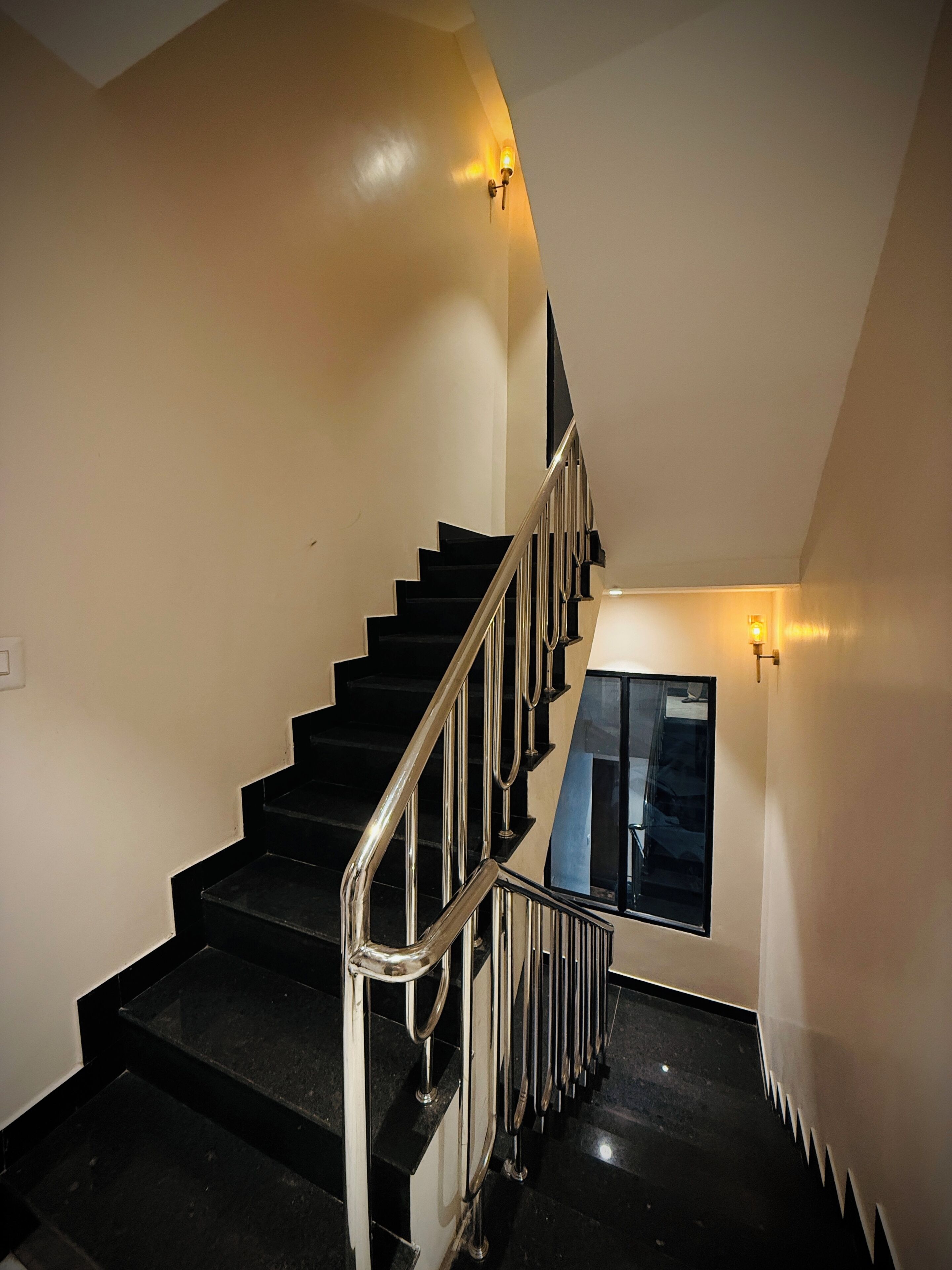 A staircase with black steps and a metal railing, leading to a landing with a window.