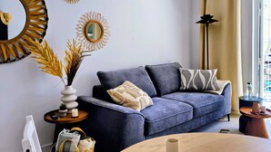 Een moderne woonkamer met een bank, een ronde houten tafel, een wandairconditioner en decoratieve spiegels.