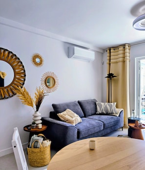 A modern living room with a sofa, a round wooden table, a wall-mounted air conditioner, and decorative mirrors. - Ocean View Terrace, Pool & Bar, Golf Del Sur 1-Bedroom Apartment (Amarilla Golf)