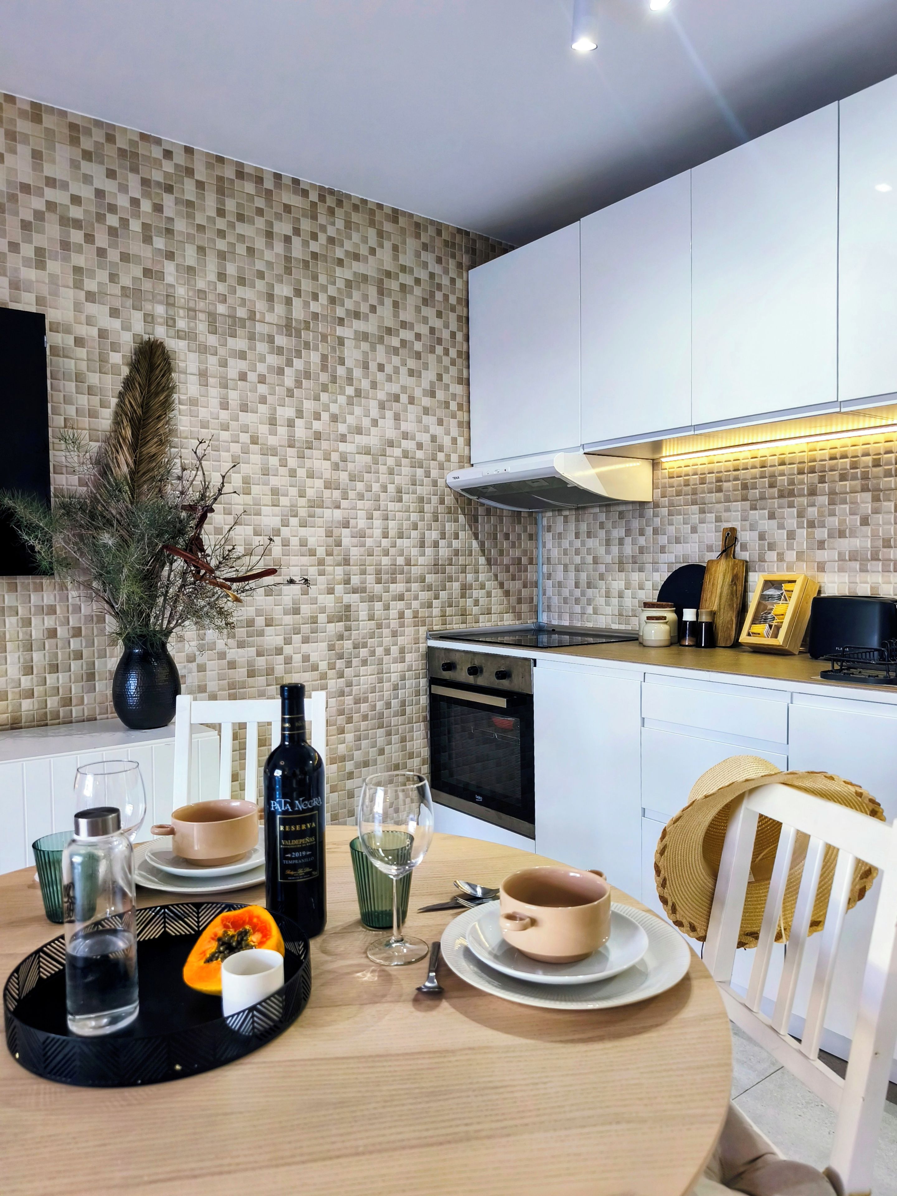 A modern kitchen with white cabinets, a tiled backsplash, and a dining area with a round table set for two.