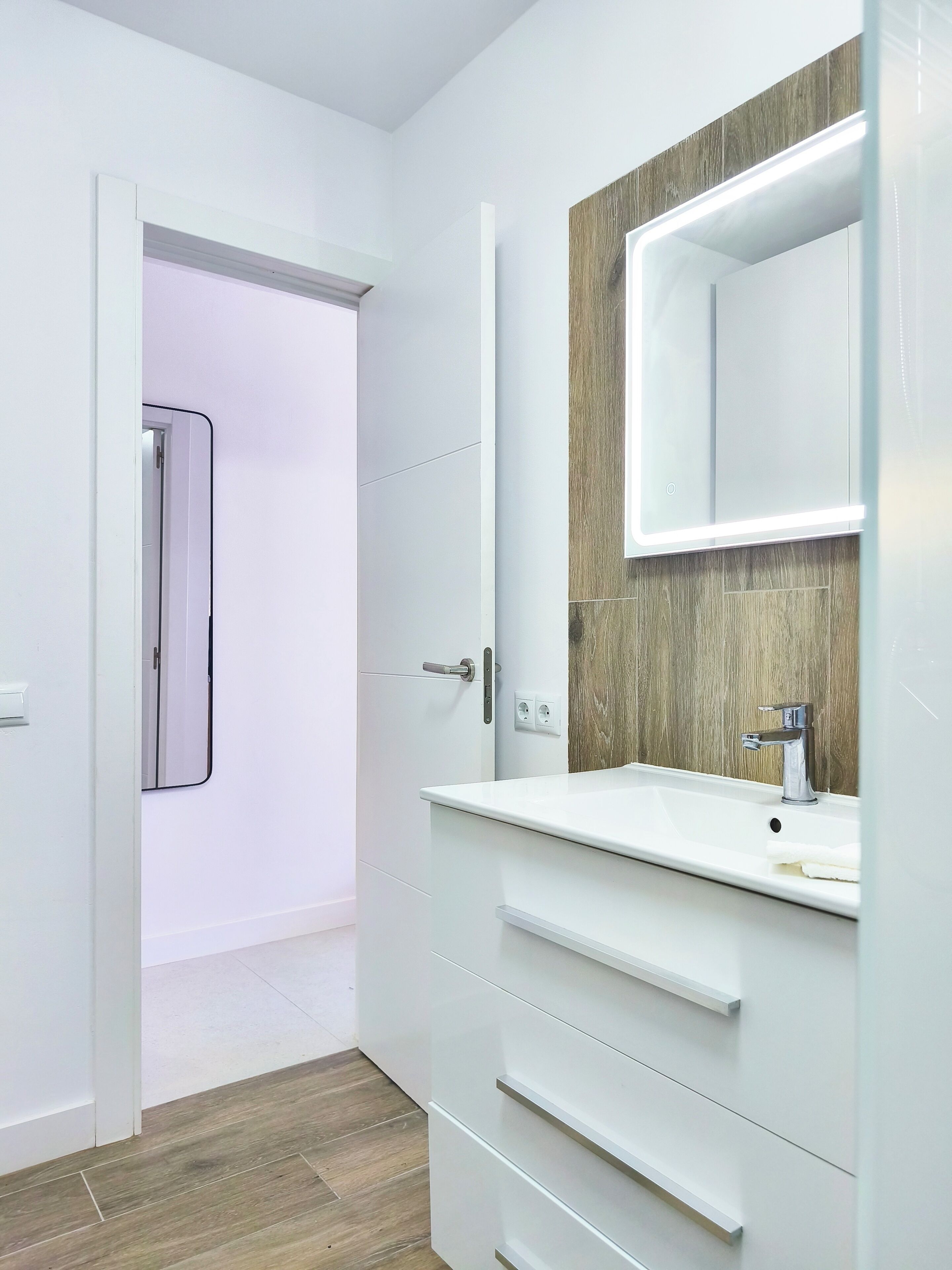 A modern bathroom with a white vanity, a mirror with a wooden accent, and a shower area.