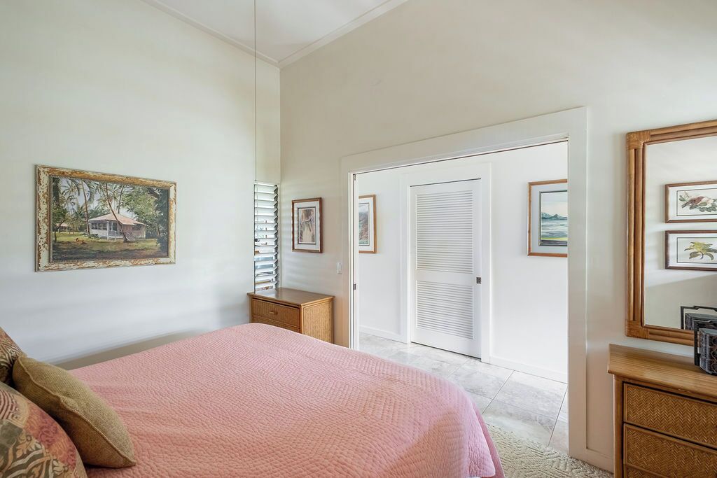 A bedroom with a bed, a dresser, a door leading to another room, and framed pictures on the wall.