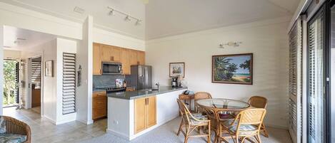 A modern kitchen with wooden cabinets, a central island, and a dining area with wicker chairs.
