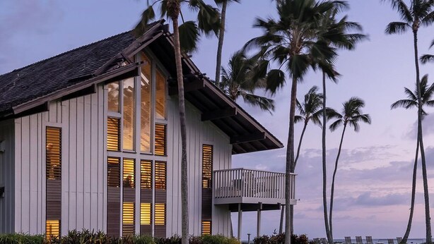 Un bâtiment situé sur la côte, doté d’un balcon, entouré de palmiers et d’une pelouse verdoyante.
