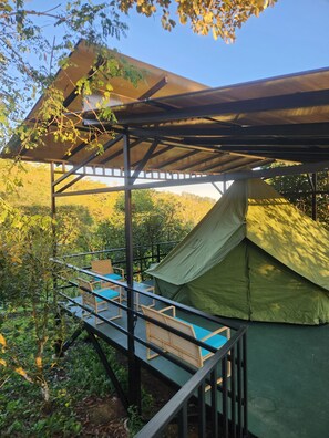Un'area campeggio con una tenda verde, una zona relax coperta con sedie, e una scala in metallo che conduce alla tenda.