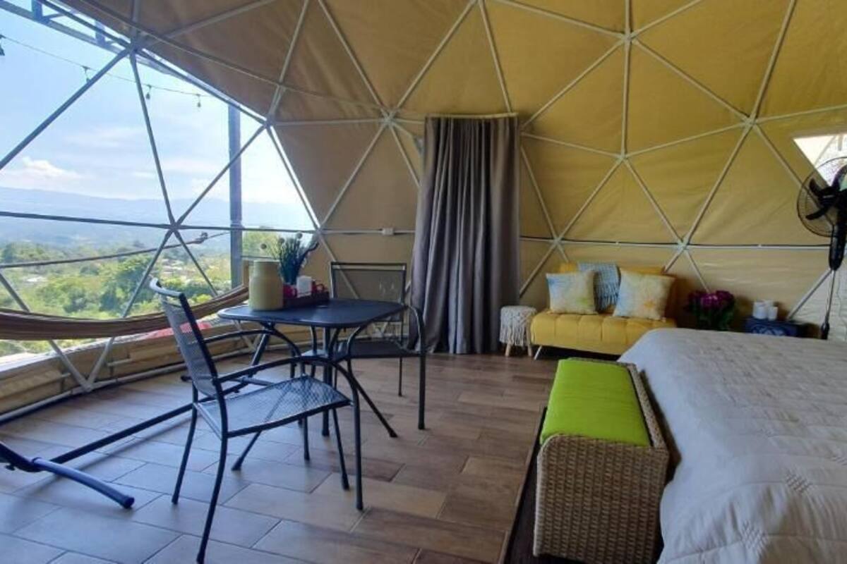 Alojamiento en tienda de campaña con zona de comedor, cama con almohadas y vistas al paisaje.
