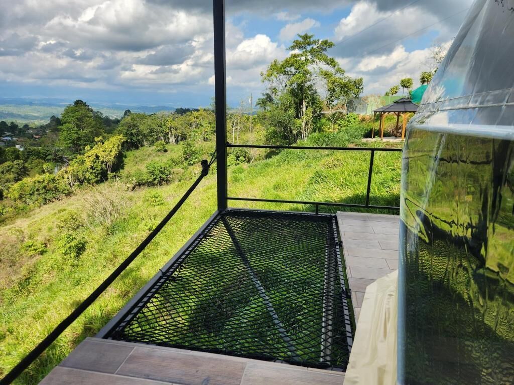 Un balcón con piso de metal que da a un paisaje verde exuberante con árboles y un cielo despejado.