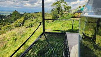 Un balcón con piso de metal que da a un paisaje verde exuberante con árboles y un cielo despejado.
