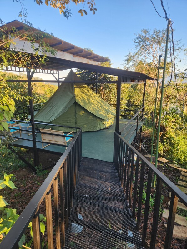 Una scala di legno conduce a una tenda verde sotto una pergola, circondata dal verde.