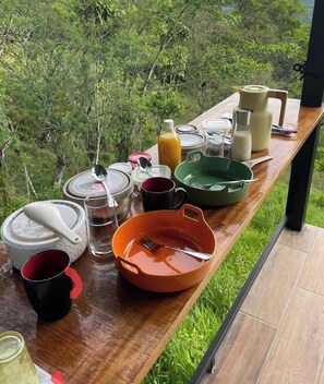 Un tavolo di legno con vari utensili da cucina e un bicchiere di succo d'arancia, sullo sfondo di un verde lussureggiante.