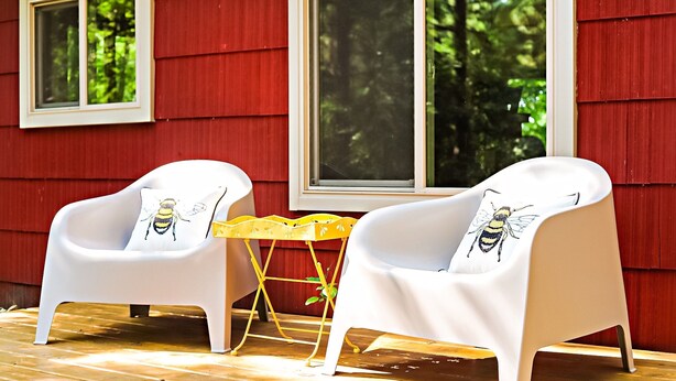 To hvide stole med puder med biedesign, et gult bord og en rød facade med vinduer.