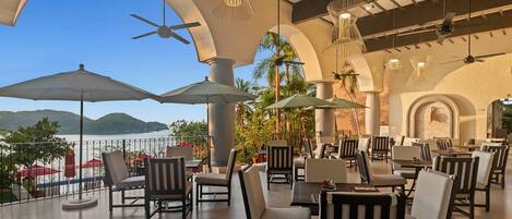 A terrace with outdoor seating, a view of the sea, and a ceiling fan.