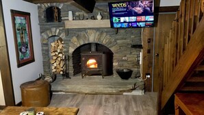 Una chimenea de piedra con un televisor que muestra la serie 'Weeds', una mesa de madera con recipientes y un interior rústico.