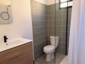 A bathroom with a white toilet, a wooden vanity, and a mirror. - Sunset Moderne Apartment - Balconies - 5 min. from Marina du Marin (Le Marin)