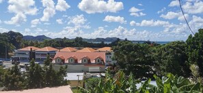 A building with a red roof, surrounded by greenery and a clear sky. - Apartment Sunset Moderne - Balconies - 5 min Marina du Marin (Le Marin)