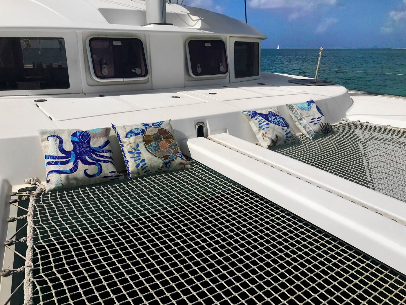 A boat deck with a netted area, cushions with blue patterns, and a view of the ocean.