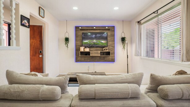 A living room with a flat-screen TV mounted on the wall, a wooden door, and a window with blinds. - Comfortable Eastside El Paso Home for Families, Nurses & Work Stays (El Paso)