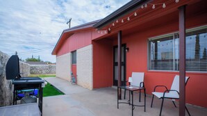 A building with a red exterior, a covered patio area with two white chairs, and a barbecue grill. - Comfortable Eastside El Paso Home for Families, Nurses & Work Stays (El Paso)
