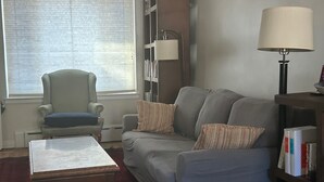 Ein Wohnzimmer mit Sofa, Sesseln, Couchtisch, Bücherregal und einer Lampe.