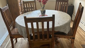 Ein runder Esstisch aus Holz mit weißer Tischdecke, umgeben von Holzstühlen, und eine Vase mit Blumen darauf.