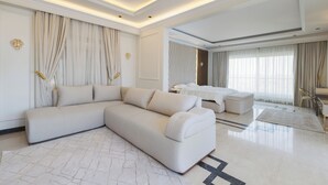 A modern hotel room with a large sofa, a bed, a desk, and a view of the city. - ALSAWAH Majestic 6BR Residence & Oasis (6th of October City)