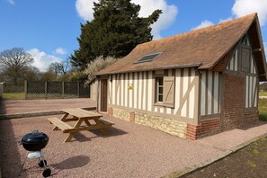 A small, single-story building with a sloped roof, a picnic table, and a barbecue grill. - Charming cottage, Pays d'Auge. Near Cabourg & Dozulé (4km). High privacy. (Putot-en-Auge)