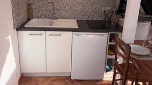 Een kleine keuken met witte kasten, een spoelbak, een vaatwasser en een eethoek met een houten tafel en stoelen.