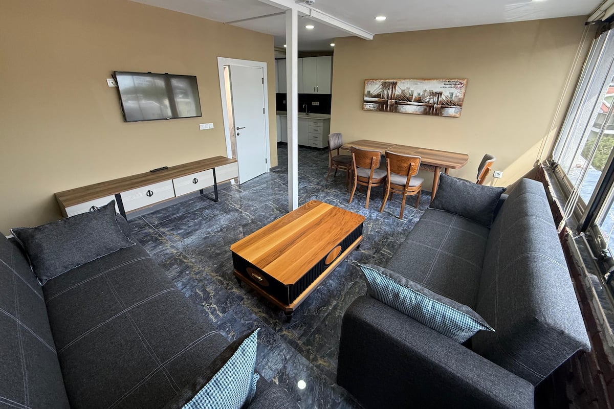 Ein modernes Wohnzimmer mit einer Sofagarnitur, einem Couchtisch, einem Fernseher und einem Essbereich mit Stühlen.